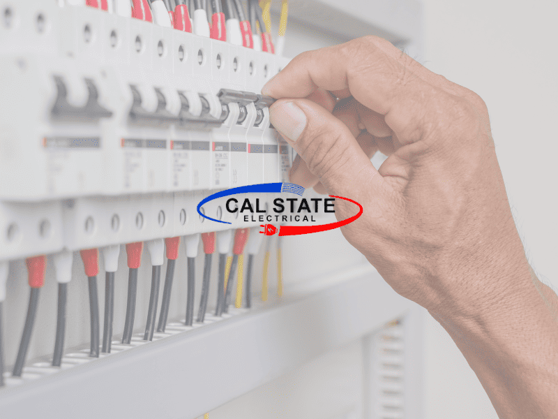 An electrician's hand working on a circuit breaker panel with wires connected to the switches, bearing the logo "CAL STATE ELECTRICAL" on the panel cover.